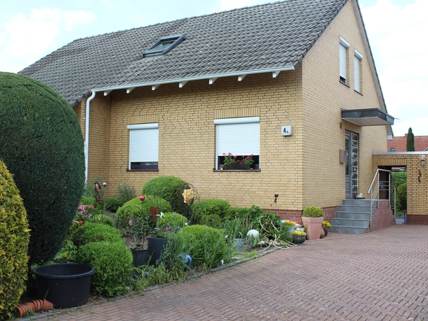 A simple detached house made of yellow clinker brick with skylight, forecourt and well-tended front garden.