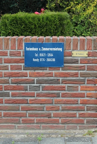 Hinweis auf Ferienhaus und Zimmervermietung, mit einer Telefonnummer auf einem gemauerten Schild.