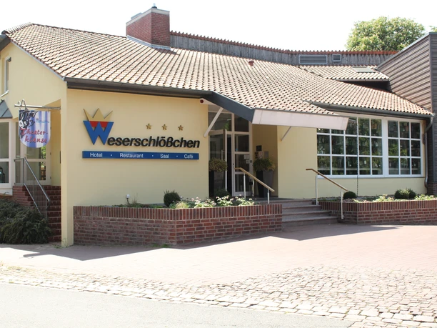 Hotel building with yellow façade and large entrance, surrounded by plants, under a blue sky.