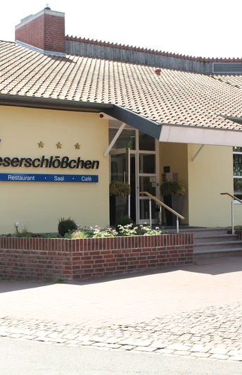 Hotel Weserschlößchen Hotelgebäude mit gelber Fassade und großem Eingang, von Pflanzen umgeben, unter blauem Himmel.
