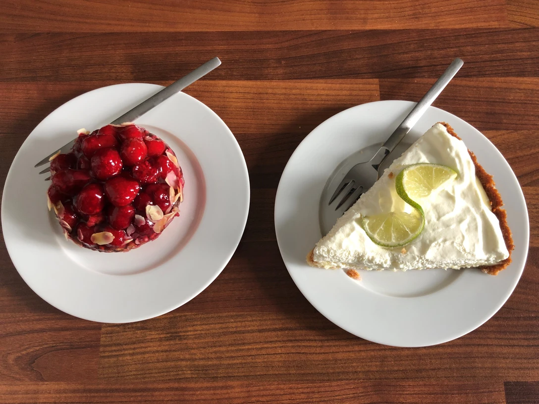 Zwei Dessertteller aus Porzellan auf Holztisch: links ein Frucht-Törtchen, rechts ein Limettenkuchen.