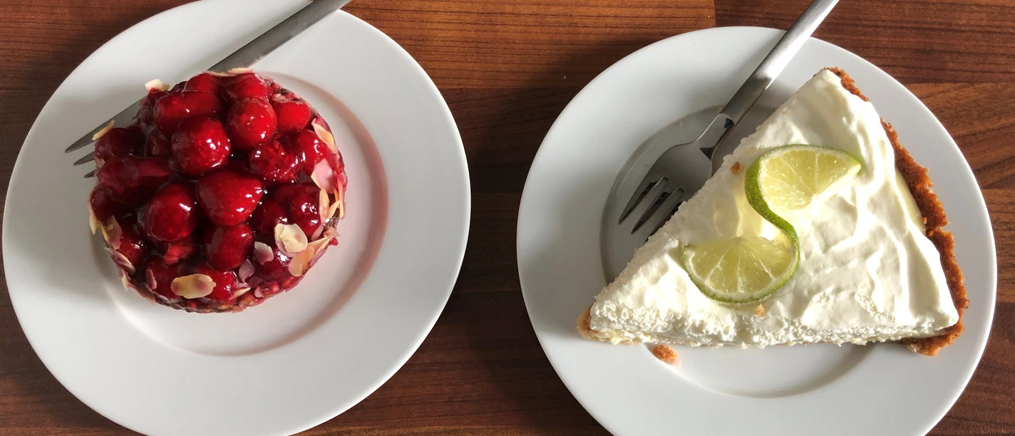 Two porcelain dessert plates on a wooden table: a fruit tart on the left and a lime tart on the right.