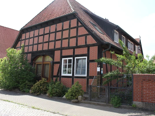 Fachwerkhaus mit rotem Ziegeldach, grossem Torbogen und gepflegtem Garten in ländlicher Umgebung.
