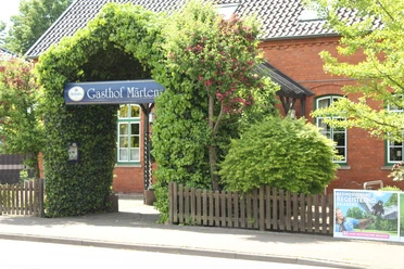 Historische herberg met weelderig groen en uitnodigende boog; rode bakstenen gevel op de achtergrond.