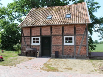 Hof Vogel Backsteinhaus mit Fachwerk, umgeben von Bäumen und Rasen, mit gepflastertem Zugang und Bank.