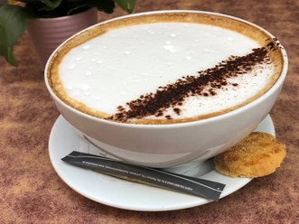 Kaffeetasse Kaffeetasse mit Milchschaum und Kakaopulver verziert, dazu ein Keks auf der Untertasse.