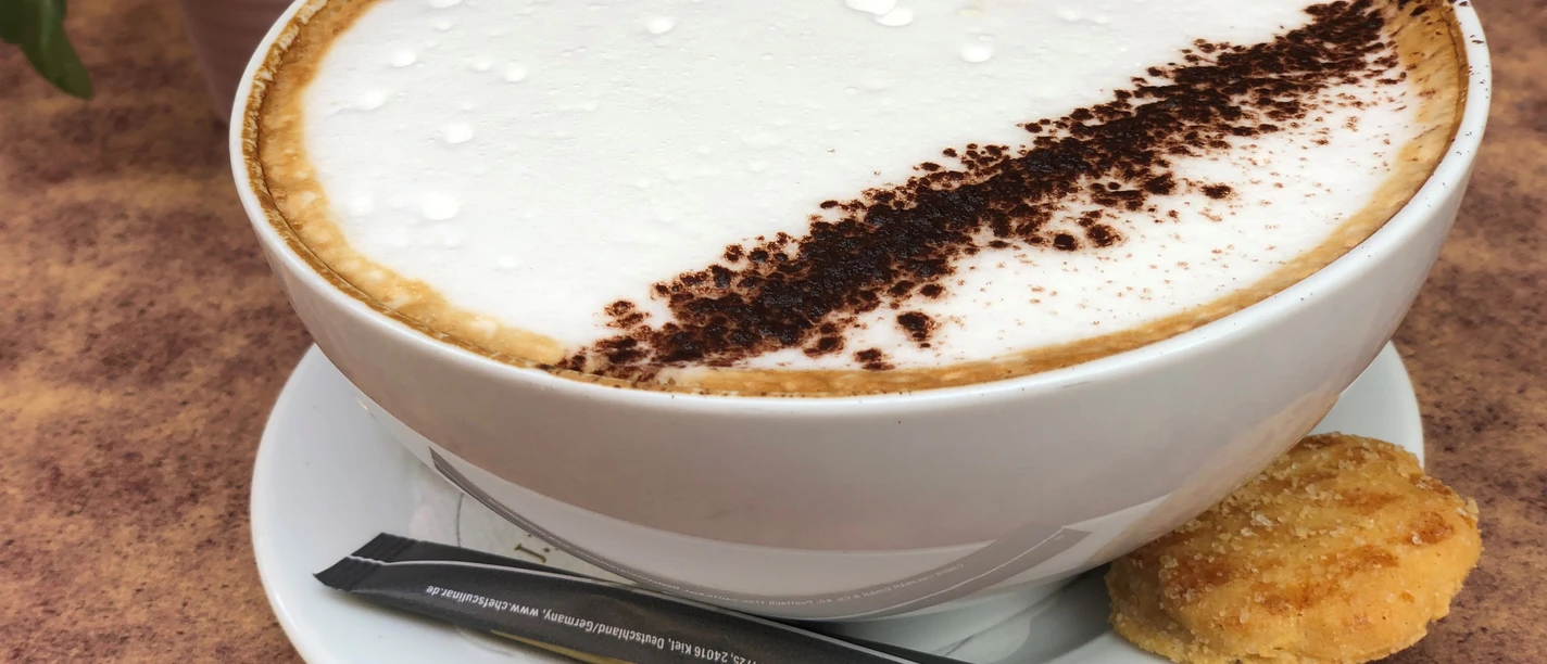 Kaffeetasse Kaffeetasse mit Milchschaum und Kakaopulver verziert, dazu ein Keks auf der Untertasse.