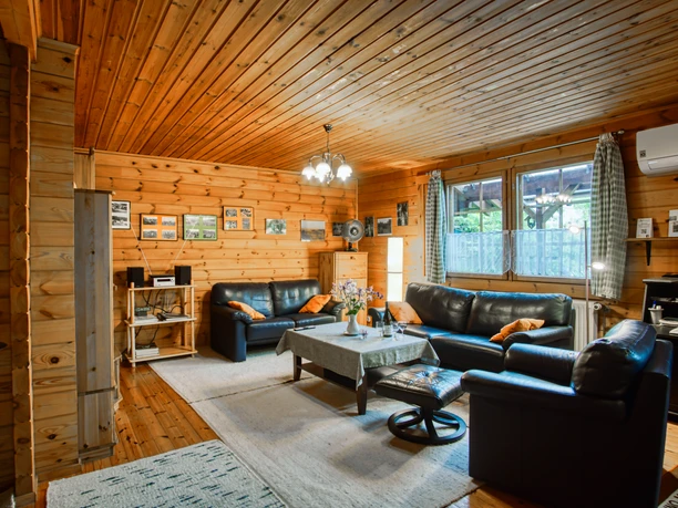 Holzgetäfeltes Wohnzimmer mit schwarzen Ledersofas, Sessel, Tisch und Fenstern.
