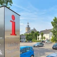 Tourist-Information Lindlar Ein Touristikinformationsschild in Lindlar, mit Kirche und parkenden Autos im Hintergrund.