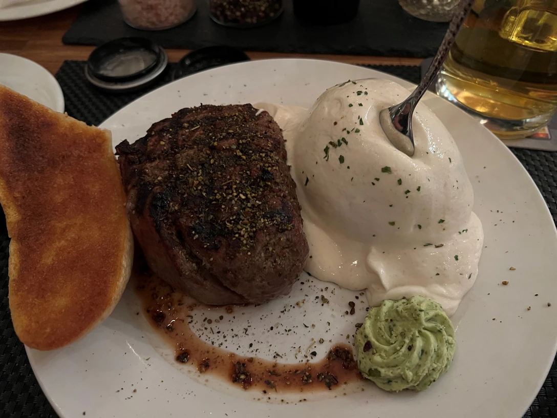 Ein saftiges Filetsteak, begleitet von einer großzügigen Portion Kräuterbutter und Brot sowie Pilzpüree.A juicy fillet steak, accompanied by a generous portion of herb butter and bread as well as mushroom puree.En saftig filetbøf, ledsaget af en generøs portion urtesmør, brød og svampepuré.Een sappige filetlap, vergezeld van een royale portie kruidenboter, brood en paddenstoelenpuree.