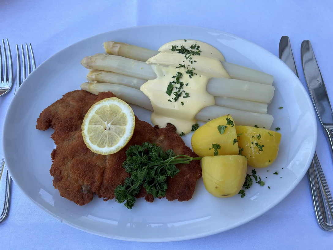 Spargelgericht Ein köstliches Gericht mit Spargel, Schnitzel, gekochten Kartoffeln und einer Scheibe Zitrone auf Weiß.