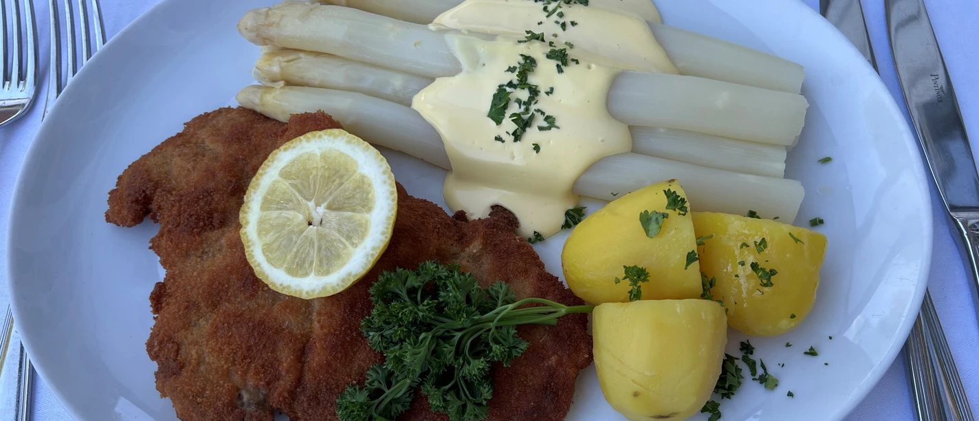 Spargelgericht Ein köstliches Gericht mit Spargel, Schnitzel, gekochten Kartoffeln und einer Scheibe Zitrone auf Weiß.