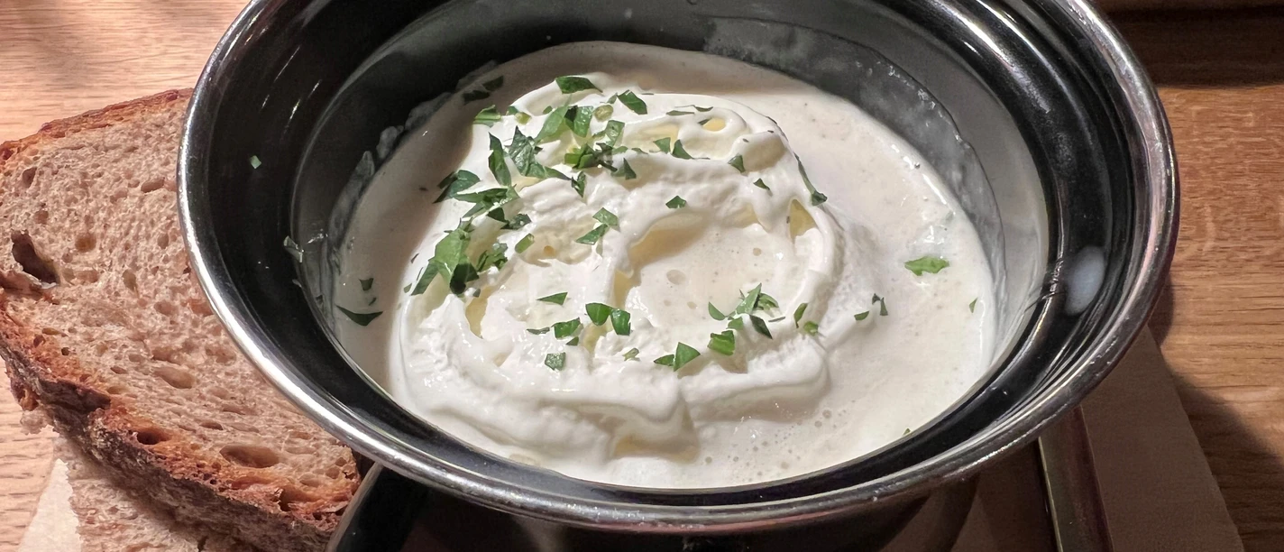 Creamy asparagus soup in a black pot, garnished with parsley, served with bread.