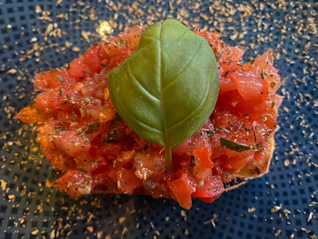 Eine knusprige Bruschetta-Scheibe mit frischen Tomatenwürfeln und einem Basilikumblatt oben drauf.