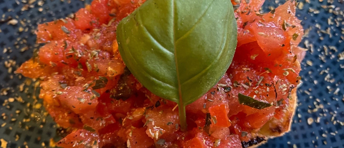 A crispy slice of bruschetta with fresh tomato cubes and a basil leaf on top.