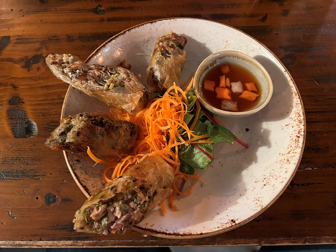 asiatisches Gericht Knusprige Frühlingsrollen, serviert mit frischen Karottenstreifen und einem Dip auf rustikalem Holztisch.