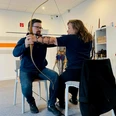 Zwei Personen sitzen drinnen, üben Bogenschießen mit traditionellem Bogen, Pfeile im Hintergrund.