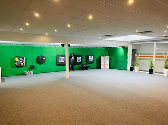 In einem modernen Innenraum befindet sich ein Bereich zum Bogenschießen mit Zielscheiben vor grünem Hintergrund.