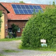 Keramik Winzlar Das Bild zeigt ein rotes Backsteingebäude mit Solarpaneelen auf dem Dach, umgeben von grüner Vegetation.