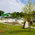 Moderner Spielplatz mit Klettergerüsten, Rutschen und Hängematten, umgeben von grüner Landschaft.