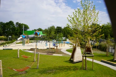 Überblick Spielgelände Moderner Spielplatz mit Klettergerüsten, Rutschen und Hängematten, umgeben von grüner Landschaft.