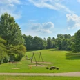 Freizeitpark (Grillplatz) Ein Spielplatz mit Schaukeln und Grünflächen in einem sonnigen Park mit blauen Himmel und Bäumen.