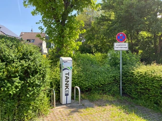 Ladesäule Kölner Straße Ladesäule für Elektrofahrzeuge zwischen grünen Hecken, daneben Parkverbots- und Reserviert-Schild.