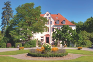 Schloss Georghausen Historische Villa mit rotem Dach, umgeben von gepflegten Gärten und blühenden Blumenbeeten.