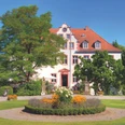 Schloss Georghausen Historische Villa mit rotem Dach, umgeben von gepflegten Gärten und blühenden Blumenbeeten.