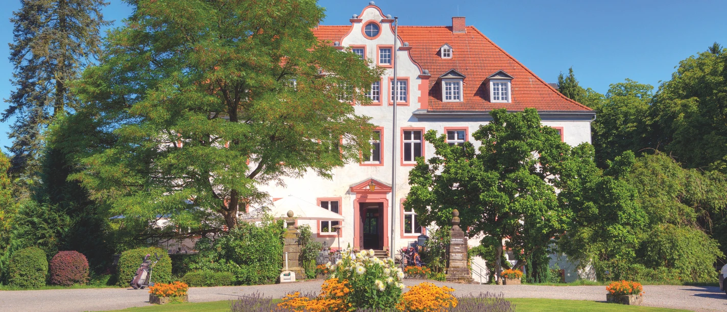Schloss Georghausen Historische Villa mit rotem Dach, umgeben von gepflegten Gärten und blühenden Blumenbeeten.