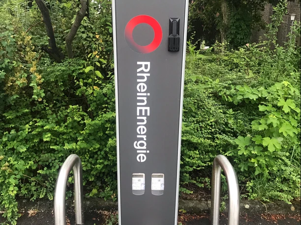 Ladesäule Linde Wanderparkplatz Ladesäule der RheinEnergie am Gehweg, umgeben von dichter grüner Vegetation im Hintergrund.
