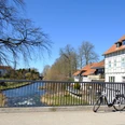 E-Bike an der Bega.JPG Ein E-Bike lehnt an einer Brücke über einen Fluss, umgeben von Fachwerkhäusern. Klarer Himmel.