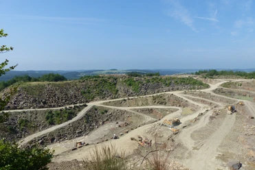 Steinbruch Lindlar Weitläufiger Steinbruch mit terrassierten Abbauflächen und Baumaschinen vor bewaldeter Hügellandschaft.