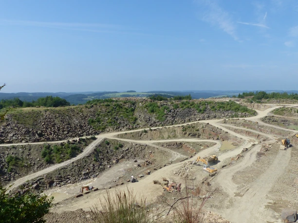 Steinbruch Lindlar Weitläufiger Steinbruch mit terrassierten Abbauflächen und Baumaschinen vor bewaldeter Hügellandschaft.