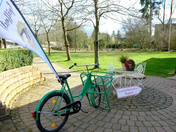 Hofladen Gutshof Brennerei Begatal.JPG Grünes Fahrrad vor einem rustikalen Backsteinbogen, daneben ein Schild zur Gutshof Brennerei Begatal.