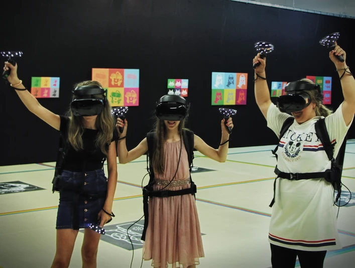 7th Space VR Langenfeld Drei Personen in virtueller Realität mit Headsets und Controllern in einem Indoor-Areal.