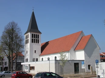 Kreuzkirche Wiedenbrück Weiße Kirche mit hohem Turm und rotem Ziegeldach, umgeben von Parkplätzen und Frühlingsbäumen.