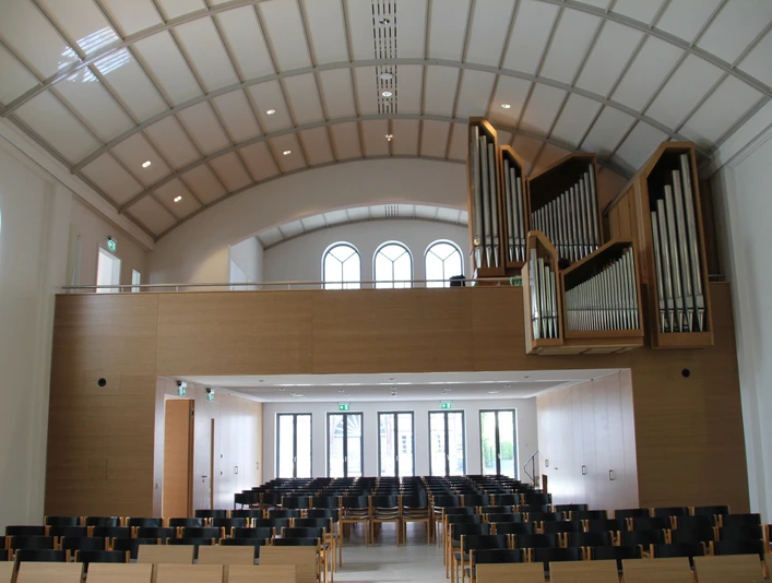 Kreuzkirche Wiedenbrück Moderner Kirchenraum mit geschwungenem Dach, Orgel links, hellem Holz, leeren Stuhlreihen und Fenstern.
