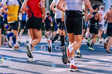 Brunnenlauf Teilnehmer eines Stadtlaufs in bunter Sportkleidung, von hinten fotografiert, umgeben von Seifenblasen.
