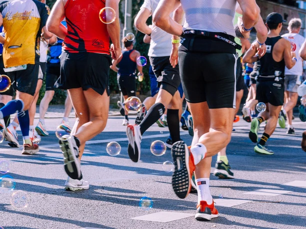 Brunnenlauf Teilnehmer eines Stadtlaufs in bunter Sportkleidung, von hinten fotografiert, umgeben von Seifenblasen.