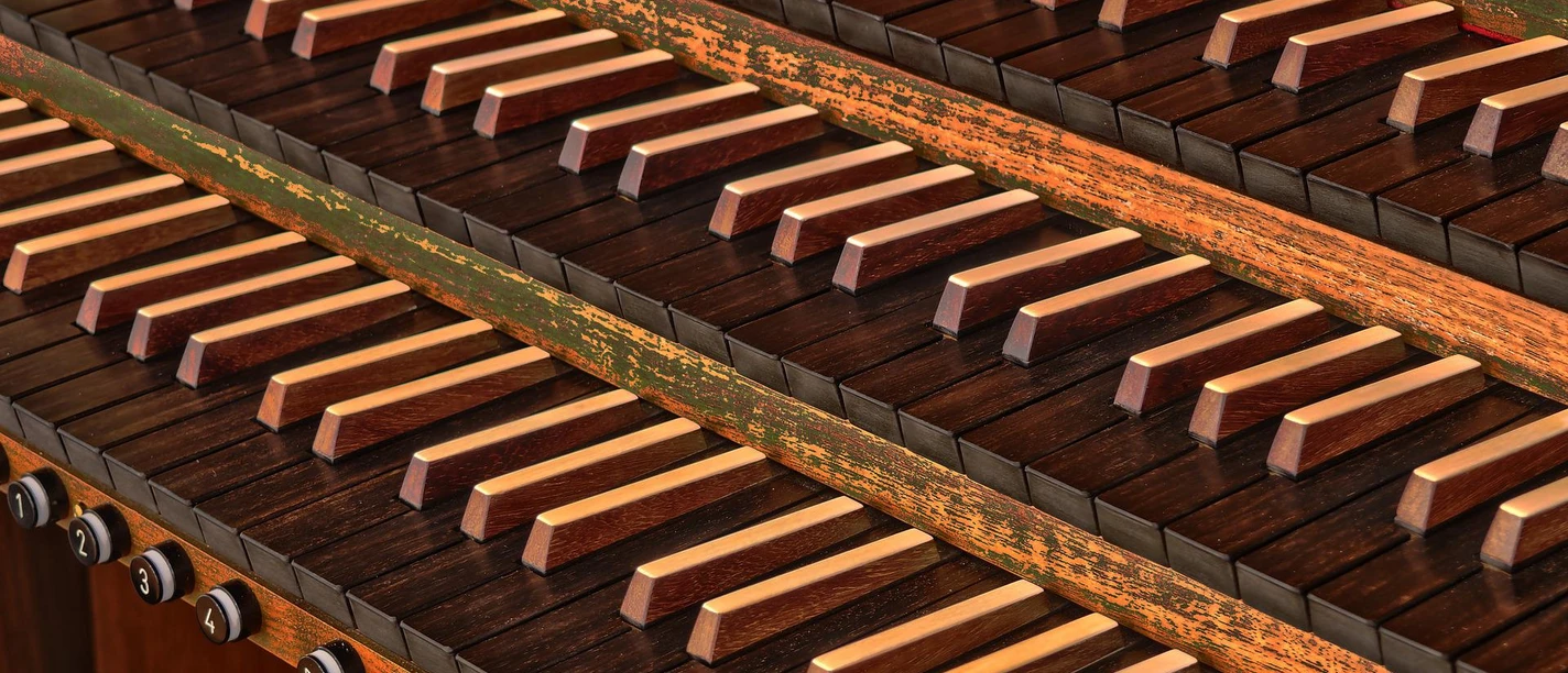 Orgel Nahaufnahme von Orgelmanualen mit holzbesetzten Tasten und eleganten Registerzügen darunter.