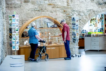 Altenberger Dom-Laden Ein älteres Paar betrachtet Ausstellungsstücke in einem Dom-Laden, er zeigt auf religiöse Artikel.