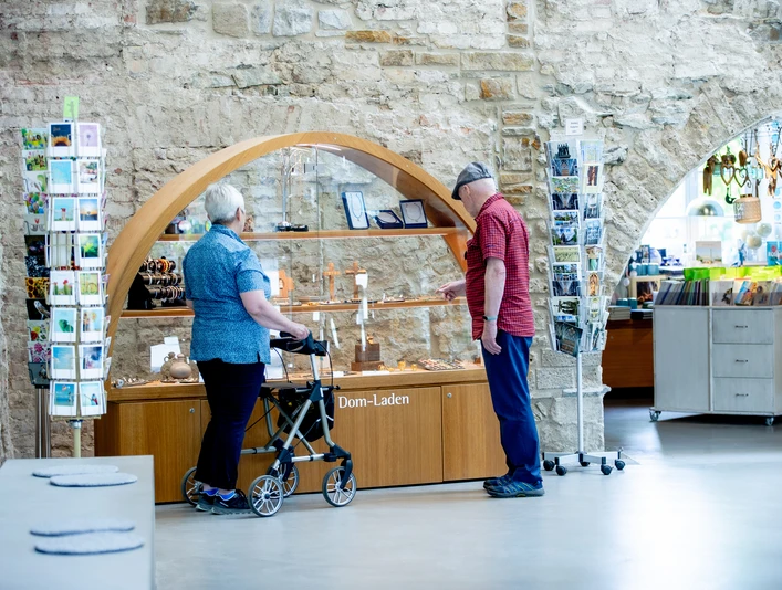 Altenberger Dom-Laden Ein älteres Paar betrachtet Ausstellungsstücke in einem Dom-Laden, er zeigt auf religiöse Artikel.