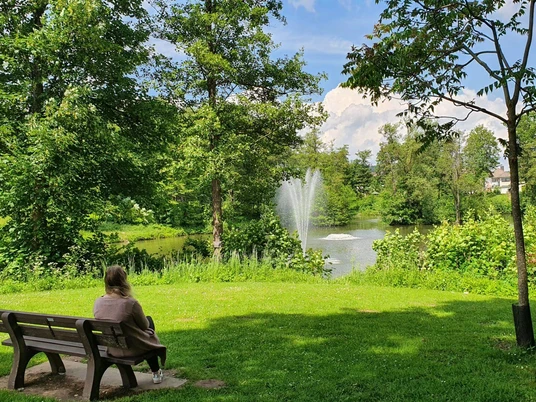 Parkbank mit einer Frau, die den Blick auf den Ententeich hat.