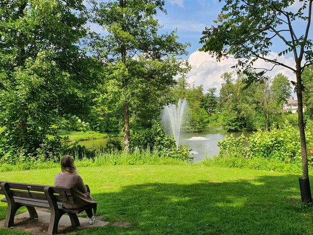 Parkbank mit einer Frau, die den Blick auf den Ententeich hat.
