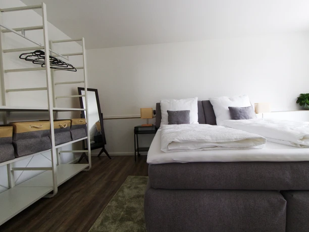 Ferienwohnung Wiehl großes Schlafzimmer.jpg Modern eingerichtetes Doppelzimmer mit Boxspringbett, Kleiderschrank, Spiegel und Nachttischen.