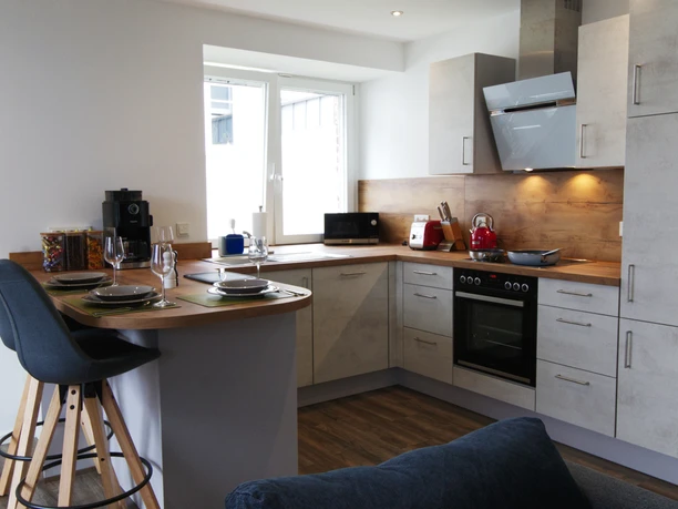 Ferienwohnung Wiehl vollausgestattete Küche.jpg Moderne, helle Küche mit Esstresen, ausgestattet mit Herd, Dunstabzug und Küchenutensilien.