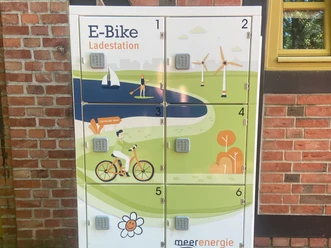 E-bike charging station with six lockers in front of a red brick wall with a wooden-framed window.