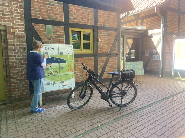 Eine Person steht vor einer E-Bike-Ladestation auf einem gepflasterten Weg neben einem Gebäude.