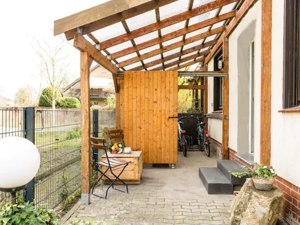 Überdachte Terrasse mit Holzmöbeln, Blumentopf und Fahrrädern; ruhige, einladende Atmosphäre.